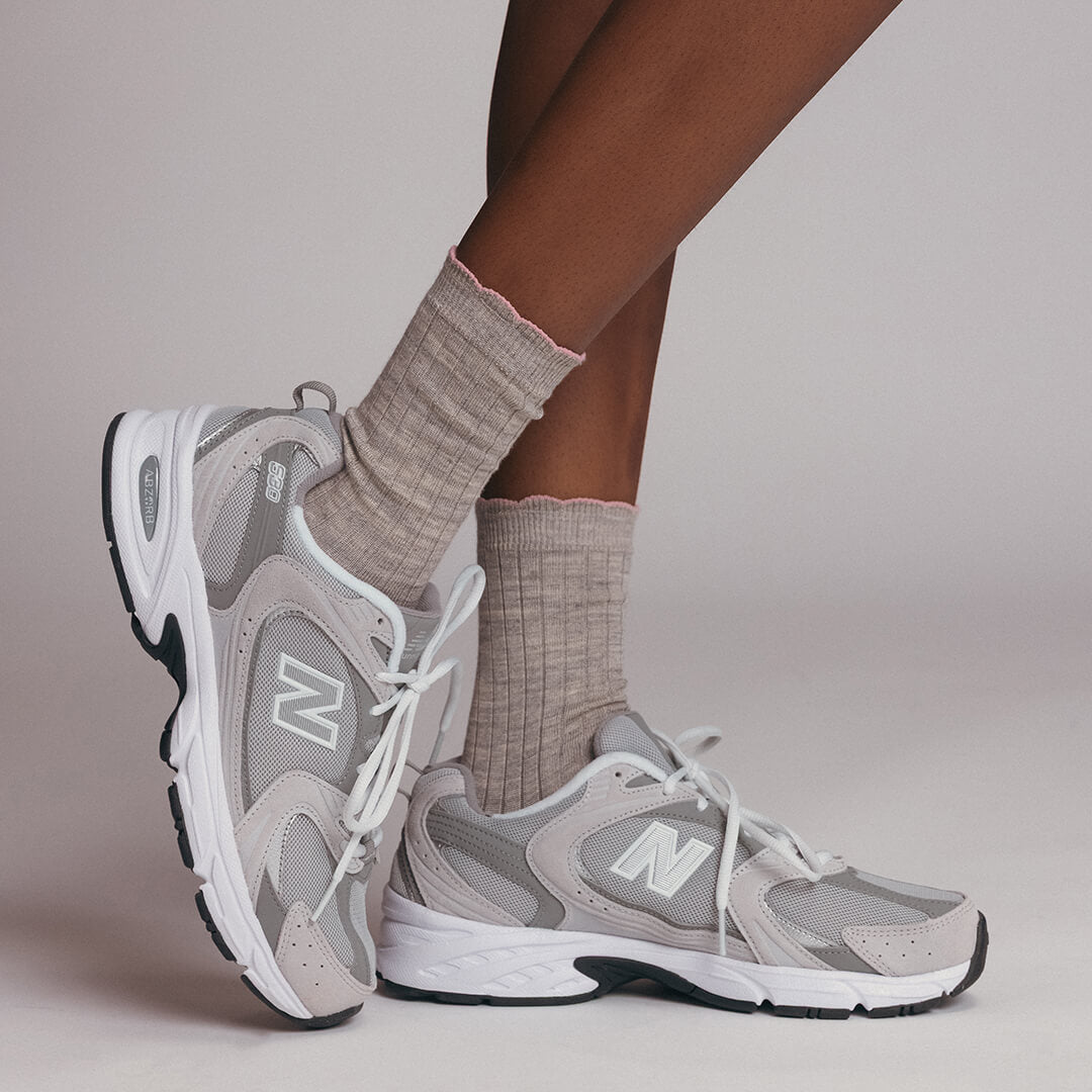 Gray sneakers with a New Balance logo worn with beige socks on a neutral background