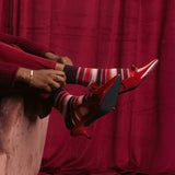 Person wearing red high-heeled shoes and striped socks sitting on a pink couch against a red curtain. thumbnail