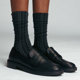 Black leather shoes with textured black  pointelle socks on a light gray background thumbnail