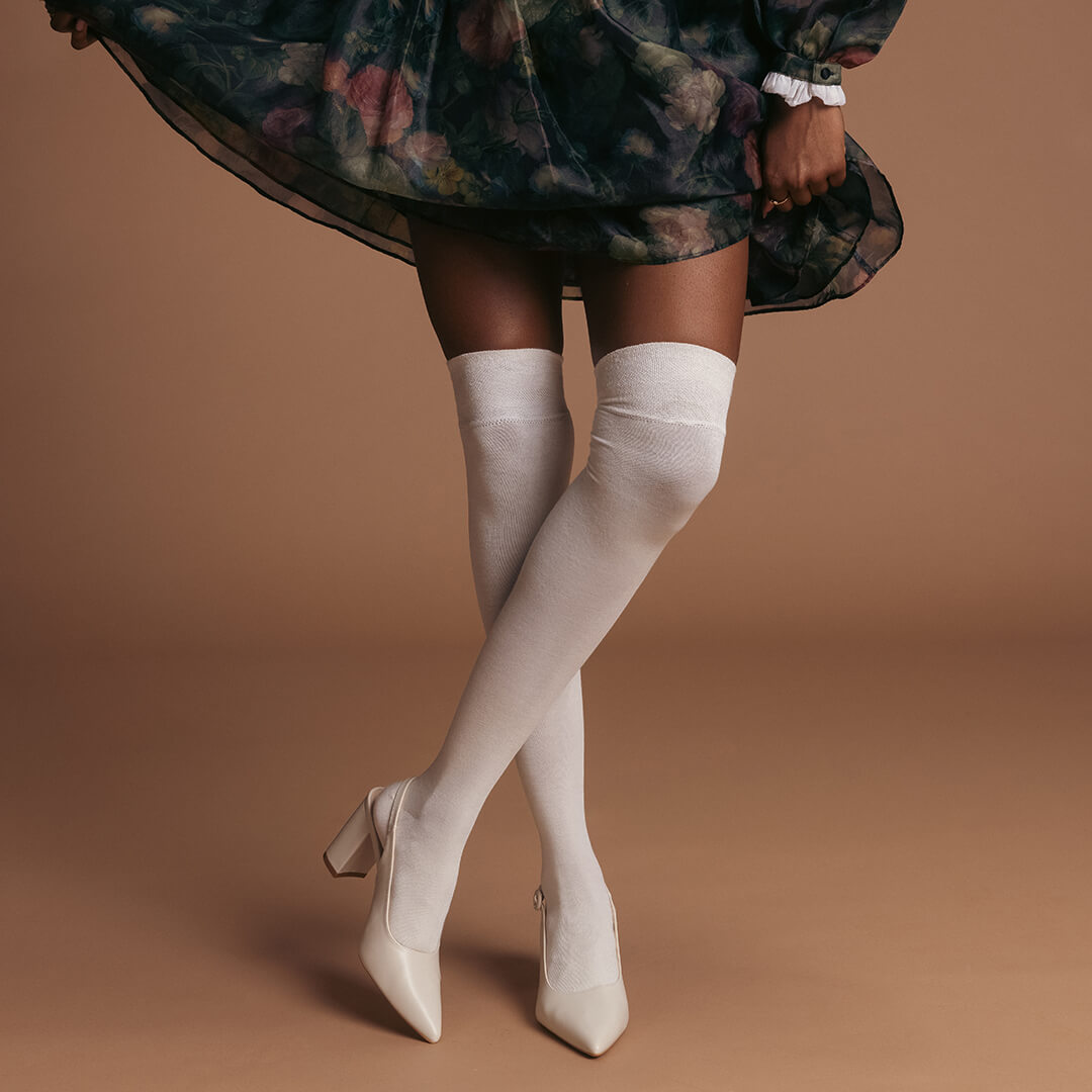 Person wearing a floral dress, white knee-high socks, and high-heeled shoes on a brown background