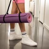 Person holding a purple yoga mat with white sneakers and pink shorts in a locker room. thumbnail