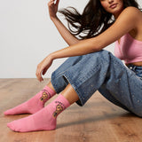 Woman wearing pink socks with the phrase "Women Unite," sitting on a wooden floor. thumbnail