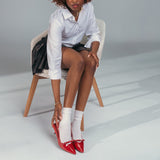 Woman sitting on a chair wearing a white shirt, black skirt, white socks, and red high heels. thumbnail