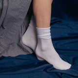 White socks worn on a person's feet with a checkered dress and blue velvet in the background