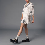 Woman wearing a white lace dress and socks with matching black floral accents on a gray background thumbnail