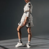 Woman wearing a white lace dress and socks with matching black floral accents on a gray background